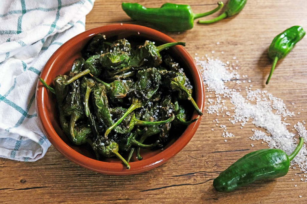 Pimientos de Padrón are small green peppers, fried in olive oil and sprinkled with coarse sea salt. Most are mild, but occasionally, you'll bite into one that’s surprisingly hot, making eating them a bit of a gamble. These peppers come from the town of Padrón in Galicia and are typically served as a tapa or a side dish.